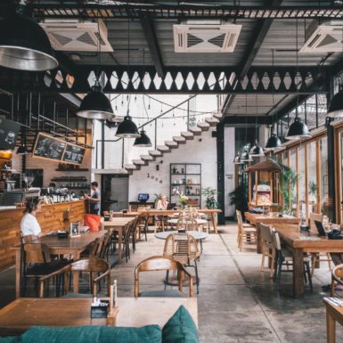 Spacious, modern café with wooden furniture, large windows, and people working or relaxing inside